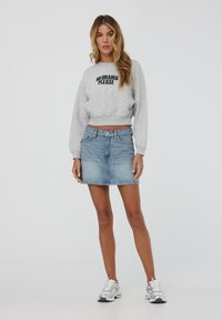 Dollino grigio corto con la scritta "NO DRAMA PLEASE", abbinato a una gonna di denim azzurro. Il modello indossa sneakers argentate.