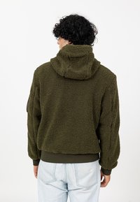 Olive green, polarowa bluza z kapturem o teksturowanej powierzchni, z kapturem i ściągaczami u dołu rękawów. Posiada luźny krój i boczne szwy.