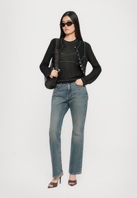 Pulover negru tricotat cu detalii de cusătură în contrast, combinat cu blugi decolorati de nuanță albastră și tocuri deschise maro. Accesoriile includ ochelari de soare negri.