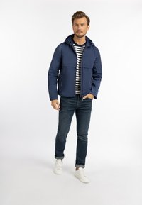 Mørkeblå hættejakke med lynlås foran, to sidelommer og en glat overflade, parret med en sort-hvid stribet skjorte og jeans.