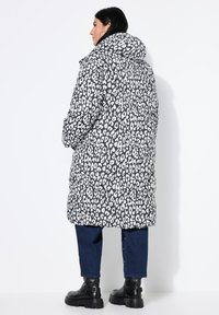Abrigo acolchado con un estampado de leopardo en blanco y negro, capucha y mangas largas. Combinado con jeans de mezclilla oscuros y botas negras gruesas.