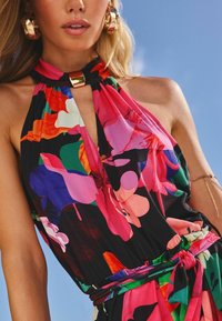 Vestido halter de patrón floral colorido, hecho de una tela ligera. Presenta un diseño de ojal y una cintura fruncida con un lazo a juego.