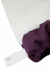 Lila Stoff mit gerafftem Rand, bedeckt von flauschigem weißem Fleece. Inklusive eines weißen Etiketts zur Personalisierung. Insgesamt weiche Textur.