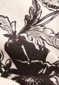 Tissu noir et blanc avec des motifs floraux et feuillus détaillés, montrant la texture et les plis du matériau.