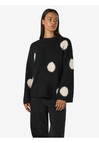 Jersey de punto negro con lunares blancos, escote redondo y mangas largas. Textura suave y ajuste holgado con dobladillo recto.