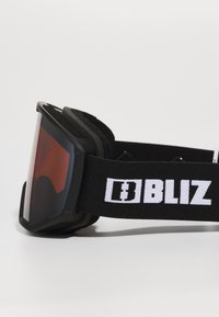 Lunettes de ski noires avec un grand verre teinté rouge, rembourrage en mousse douce et une sangle noire avec une marquage "BLIZ" blanc.