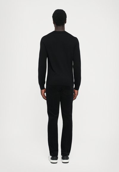 Black knitted sweater with long sleeves and a crew neck, paired with dark pants and white-accented sneakers; simple and classic design.
