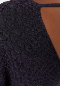 Navyblauw gebreid top met een gemarmerd, schubachtig patroon. Heeft een open rug met een dunne band om de nek voor extra detail.