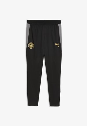 Czarne spodnie sportowe z szarymi panelami bocznymi, z złotym logo Manchester City na lewym udzie oraz złotym logo Puma na prawym udzie.