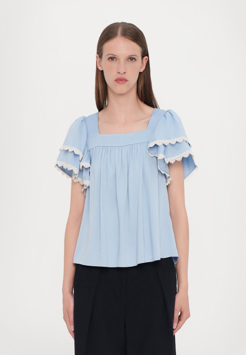 Blusa azzurro chiaro realizzata in tessuto morbido, con maniche corte a palloncino bordate in pizzo bianco e scollatura quadrata, con pieghe arricciate.