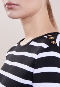 Svart och vit randig topp med rund halsringning, prydd med tre guldknappar på axeln. Slät textil med en figurnära design.