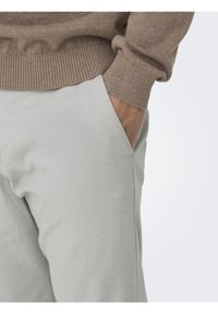 Pantalones texturizados gris claro con un corte relajado, que cuentan con bolsillos laterales y una cintura acanalada, combinados con un suéter de punto marrón.