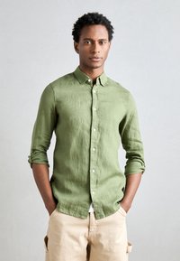 Cămașă din in verde cu un design cu nasturi, mâneci răsfrânte și nasturi albi, asortată cu pantaloni scurți bej. Textură simplă și stil casual.