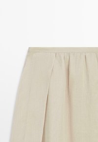 Beige linnen rok met geplooide taille en een split aan de voorkant, weergegeven op een effen witte achtergrond.