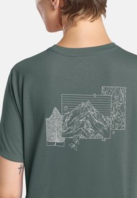T-shirt en coton vert avec un motif graphique blanc représentant des montagnes, des feuilles et des motifs rectangulaires au dos. Manches courtes, col rond.