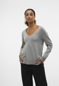 Pull gris à manches longues avec un col en V, des poignets et un ourlet côtelés, comportant deux poches latérales. Texture lisse, design décontracté.