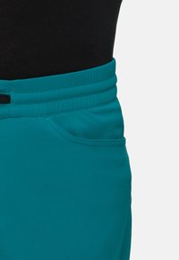Teal rekbare broek met een elastische tailleband, zijzak en een gladde textuur. Bevat platte naden en een aansluitend ontwerp.