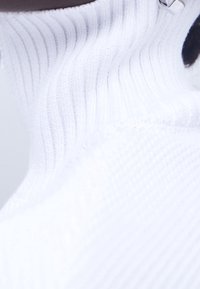 Vit stickad tröja med ribbat mönster och viks krage, som har en mjuk textur och subtil lyster. Synlig silverdetalj.