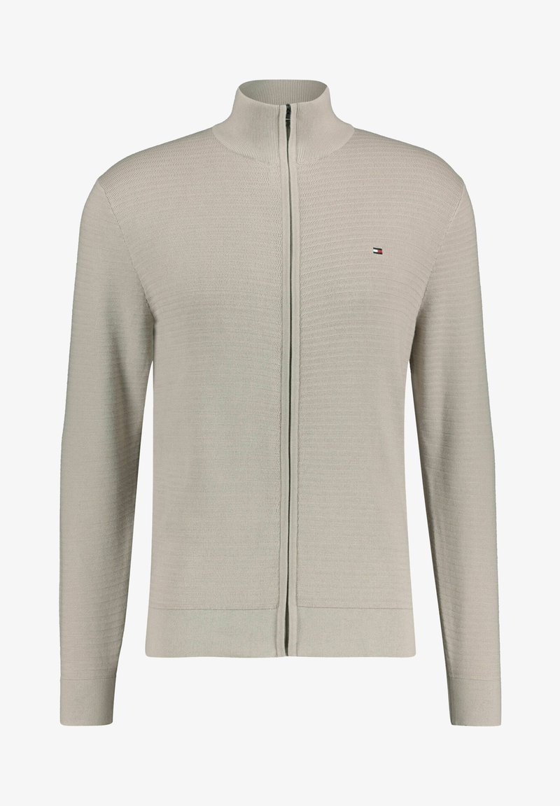 Vaaleanharmaa vetoketjullinen neuletakki, joka on valmistettu teksturoidusta neuleesta ja jossa on korkea kaulus sekä ribbaudet päätteet. Pieni logo vasemmassa rinnassa.