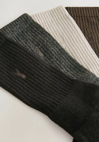 Drei Paar gerippte Socken in Dunkelgrün, Creme und Braun. Jede Socke zeichnet sich durch eine strukturierte Oberfläche und dezente Stickdetails aus.