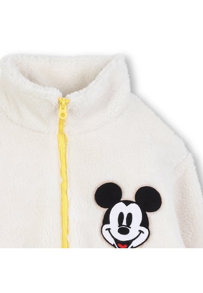 Veste polaire blanche avec une fermeture éclair jaune, un col montant et un appliqué Mickey Mouse noir et blanc sur la poitrine. Texture douce.