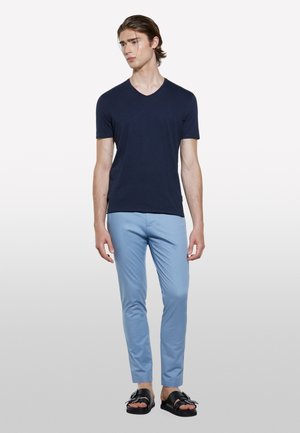 T-shirt bleu marine en V en tissu doux, assorti à un pantalon slim fit bleu clair et des sandales noires avec un détail de boucle.