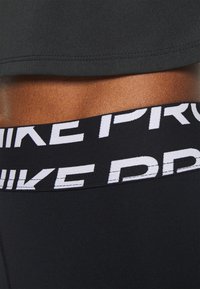 Black athletic top with a cropped design. Features a wide black waistband with white “NIKE PRO” text. Smooth texture, fitted shape.