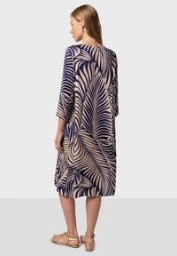 Flowy knee-length dress in navy blue with beige palm leaf pattern, featuring three-quarter sleeves and a loose fit, made of soft fabric.