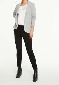 Blazer gris à manches longues, deux boutons et coupe structurée, associé à un pantalon skinny noir et des bottines à talons noires.