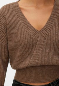 Pull en maille côtelée marron avec encolure en V, manches longues et taille cintrée, porté par une personne portant un pantalon noir.