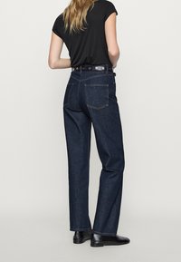 Jean en denim bleu foncé avec une coupe ample, dotés de deux poches arrière, de détails en point de chaînette et d'une taille avec passants de ceinture.