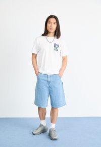 Hvit t-skjorte med kort erme og grafisk trykk, lyseblå denimshorts, grå joggesko og hvite ankelsokker. Enkel design.