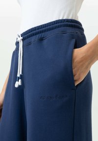 Donkerblauwe joggingbroek van zacht materiaal, met een elastische tailleband met witte trekkoord, zijzakken en subtiele geborduurde tekst.