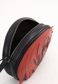 Borsa rotonda in pelle nera con design a fiamma rossa. Caratterizzata da una chiusura zip e una tracolla regolabile. Interno foderato in materiale morbido.