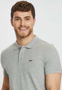 Polo de manga corta gris con tapeta, dos botones y un pequeño logo bordado burdeos en el pecho. Textura suave.