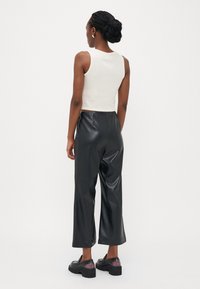 Hvid, ribbet tanktop og sorte, brede bukser i imiteret læder. Sorte kraftige loafers med detaljer i gennemsigtigt hæl. Ensfarvet baggrund.