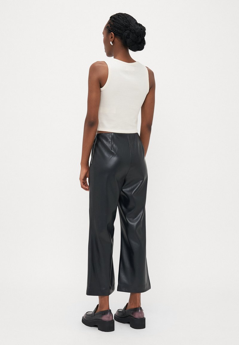 Bílý žebrovaný top bez rukávů a černé široké kalhoty z umělé kůže. Černé robustní mokasíny s průhledným detailním podpatkem. Jednoduché pozadí.