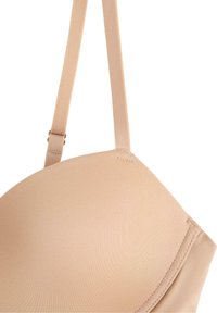 Soutien-gorge beige sans couture, avec un tissu lisse, des bonnets moulés, des bretelles réglables et un léger brillant. Les bords cousus offrent un renforcement.