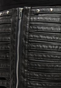 Zwarte leren rok met verticale plooien, zilverkleurige metalen ritssluiting en drukknopen aan de tailleband. Getextureerd met een gladde afwerking.