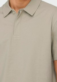 Lys grå polo t-shirt med en struktureret vævning, der har en standard krave, en-knaps lukning og korte ærmer med lige sømme.