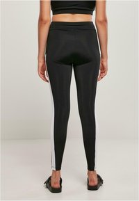 Fekete leggings fehér oldalsávokkal, rugalmas anyagból készült. Magas derékú kialakítás, testre simuló forma, sima textúra és minimális látható varratok.