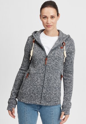 Gray knit zip-up hoodie with a hood, drawstring accent, and brown hardware. Worn over a white t-shirt and paired with blue jeans.