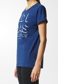 Blå bomulls t-shirt med v-ringning och korta ärmar, med fet vit text "ADIDAS ATHLETICS" på framsidan. Slät struktur.