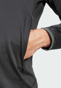 Camisola masculina preta de manga longa com um bolso com zíper na lateral e uma manga cinza. O tecido é suave com um leve stretch.