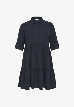 Námořnická modrá, šaty košilového střihu do kolen vyrobené z lehkého materiálu. Obsahují límeček na knoflíky, dlouhé rukávy a sukni se stupňovitým designem.