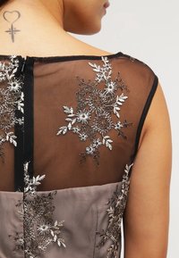 Šaty bez rukávů s černou průhlednou zadní částí zdobenou stříbrnou květinovou výšivkou; taupe korzet s texturovanou látkou, zapínání na zip.