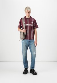 Burgunderstripet polo shirt, lyseblå slitte jeans, svarte klumpete sko og en grå crossover-veske med glidelås.