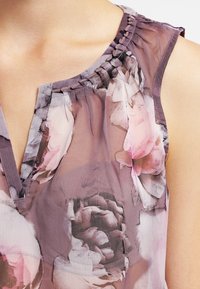 Blusa floreale trasparente con motivo di peonie rosa e grigio, scollo plisettato e texture morbida. Design a V con leggero dettaglio arricciato.