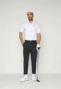 Hvit golf polo skjorte med svart Nike-logo, mørke bukser, hvite golfhansker og hvite golf sko. Holder en golfsleiv, og har på seg en hvit caps.