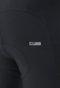 Leggings de sport noirs en matériau synthétique lisse, avec un patch logo argenté et des détails de couture contrastants.